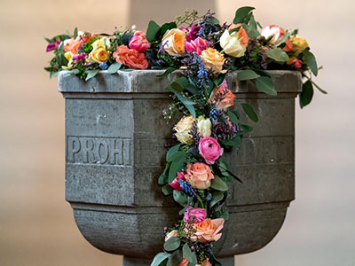 Taufbecken in einer Kirche mit Blumenschmuck. (c) Foto: Pixabay