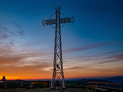 Metallkreuz vor einem sonnengefärbten Nachthimmel. (c) Foto: Pixabay