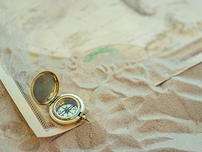 Auf einer mit Sand bedeckten Landkarte liegt ein kleiner, goldener Kompass. (c) Pexels
